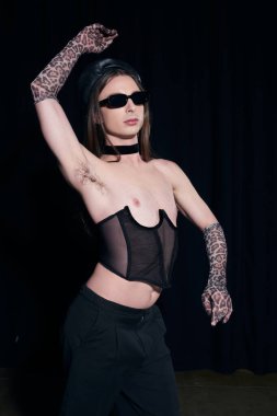Modayı takip eden uzun saçlı, şık korseli, güneş gözlüklü ve eldivenli eşcinsel adam siyahların izole edildiği bir partide LGBT onur ayını kutlarken poz veriyor. 