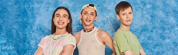 Overjoyed young homosexual community looking at camera together while celebrating lgbt pride month and standing on mottled blue background, banner