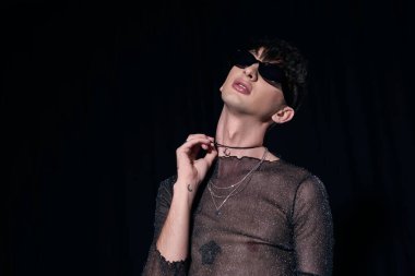 Güneş gözlüklü, ışıl ışıl parlayan kolyeli bir gay. Igbt cemaati ve onur ayı partisi sırasında siyahlar üzerinde izole edilmiş. 