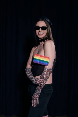 Kaygısız ve uzun saçlı, güneş gözlüklü, seksi tişörtlü ve eldiven giymiş eşcinsel adam. Gurur aylarında elinde lgbt bayrağı tutuyordu.