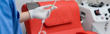Doktorun steril lateks eldivenli görüntüsü. Kan bağışı merkezinde, bulanık otomatik ekipman ve tıbbi sandalye yanında kan nakli ayarlı.