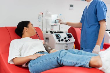 Mavi üniformalı sağlık çalışanı ve lateks eldivenli, laboratuara kan bağışlayan çok ırklı bir kadının yanında otomatik kan nakli makinesi.
