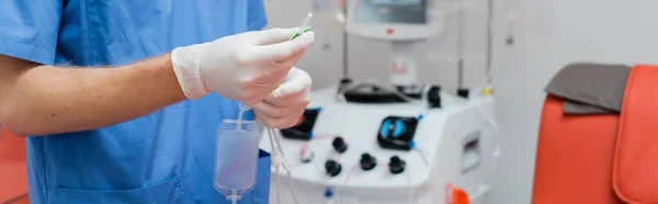 穿着蓝色制服和乳胶手套 手持输血装置 在自动化设备附近 在诊所 横幅模糊背景下 在医疗椅边模糊的医生偏视 — 图库照片