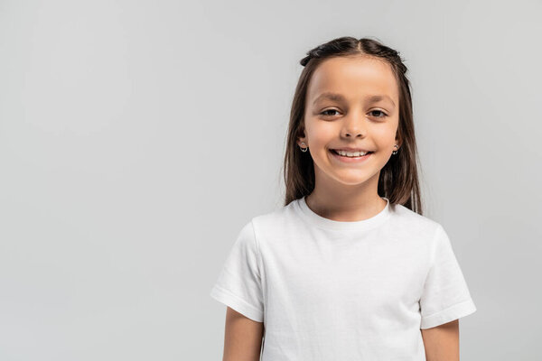 Portrait of smiling preteen and brunette girl in white t-shirt looking at camera while celebrating global child protection day isolated on grey with copy space
