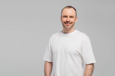 Tıraşsız, mutlu ve beyaz tişörtlü bir adam stüdyoda gri arka planda poz verirken kameraya bakıyor, kopyalama alanı, mutluluk 