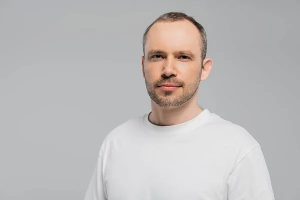 stock image unshaved man with bristle standing in white t-shirt and looking at camera while posing isolated on grey background in studio, copy space, confidence and masculinity 