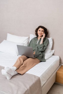 Uzun boylu ve mutlu bir kadın. Dalgalı esmer saçlı. Yatakta dizüstü bilgisayarla oturuyor ve otel odasındaki beyaz yastıkların yanında cep telefonuyla konuşuyor.