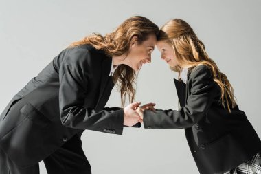 Mutlu anne ve kız el ele tutuşuyor, takım elbiseli kadın ve üniformalı kız birbirine bakıyor ve gri arka planda gülümsüyor stüdyoda, şık bir ailede, yeni okul yılında. 