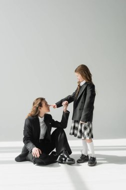 Çalışan annenin burnuna dokunan liseli kız, okul üniformalı neşeli kız gri arka plandaki iş kadınına bakıyor, resmi kıyafetler, moda ailesi, kaynaşma, modern ebeveynlik. 