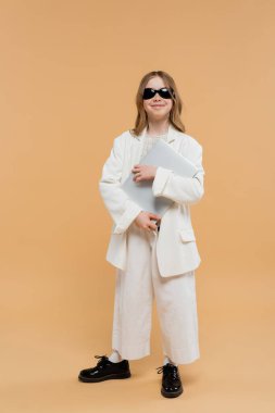 Çevrimiçi eğitim, beyaz takım elbiseli moda ergen kız, dizüstü bilgisayarlı mutlu çocuk ve bej arka planda duruyor, şık kıyafetler, resmi kıyafetler, çocuk modeli, moda belirleyici, e-öğrenme 