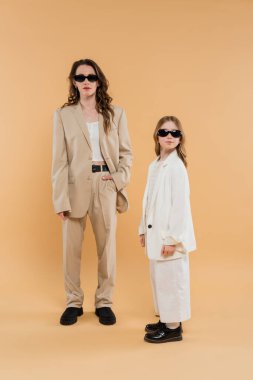Modern aile, güneş gözlüklü anne ve kız, şık iş kadını ve takım elbiseli kız bej arka planda birlikte poz veriyorlar, şık kıyafetler, resmi kıyafetler, kurumsal anne. 