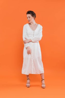 Yaz modası, beyaz elbiseli genç bir kadın turuncu arka planda dikiliyor, canlı bir arka plan, şık bir poz, beyaz giyimli bir bayan, moda modası, zarafet. 