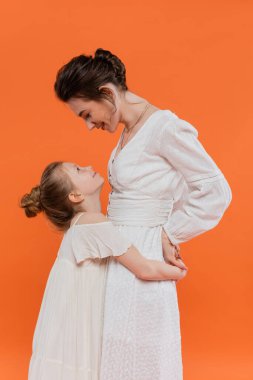 Yaz trendleri, turuncu arka planda sarılan ergen kızlar, beyaz güneş elbiseleri, birliktelik, moda ve tarz konsepti, bağlanma ve aşk, modern ebeveynlik, mutluluk. 