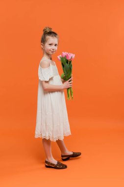 Yazlık elbise, elinde turuncu arka planda pembe laleler, moda ve tarz konsepti, çiçek buketi, şık çocuk, canlı renkler, yaz elbisesi, tam boy 