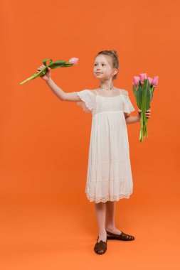 Çiçek buketi, turuncu arka planda pembe laleler tutan beyaz elbiseli küçük kız moda ve tarz konsepti, şık çocuk, canlı renkler, yaz modası, tatlı çocuk 