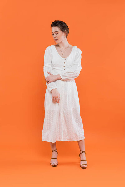 летняя мода, молодая женщина в белом солнцезащитном платье глядя в сторону и стоя на оранжевом фоне, яркий фон, стильная поза, дама в белом, мода тенденция, элегантность 