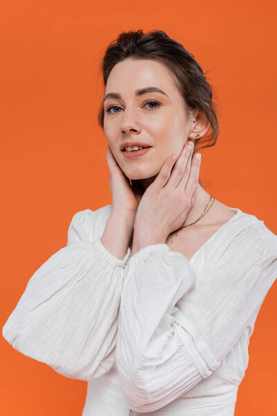 летние тенденции, чувственная молодая женщина в белом солнцезащитном платье, смотрящая на камеру и трогательное лицо на оранжевом фоне, стильная поза, дама в белом, модель, яркий фон, портрет 