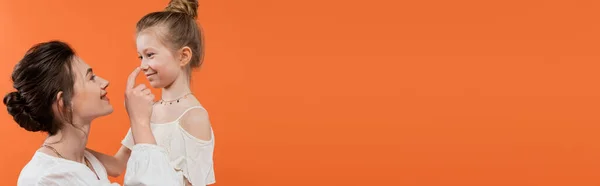 家族の絆幸せな母親がオレンジの背景に娘の鼻に触れる白い太陽のドレス現代の子育て夏のファッション一緒に愛ファッショナブルな家族バナー — ストック写真
