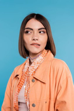 portrait of woman biting her lip, looking away on blue background, pensive, flirty, orange shirt, generation z, short brunette hair, pierced nose, summer outfit, gen z fashion, casual attire  clipart