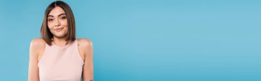 not knowing, positive young woman with tattoos and nose piercing standing in tank top on blue background, looking at camera, confused, pretty face, generation z, summer outfit, banner  clipart