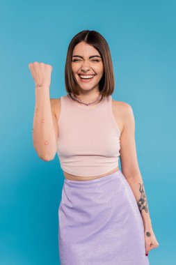 Yaz trendleri, kısa saçlı, mavi arka planda evet jesti gösteren pozitif genç kadın, günlük kıyafet, genel z moda, kişisel tarz, burun piercing, heyecan. 