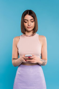 woman texting on smartphone, short hair, tattoos and nose piercing using mobile phone on blue background, casual attire, gen z fashion, personal style, everyday makeup  clipart