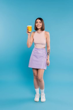 coffee to go, cheerful young woman with short hair, tattoos and nose piercing holding paper cup on blue background, generation z, summer trends, attractive, coffee culture  clipart