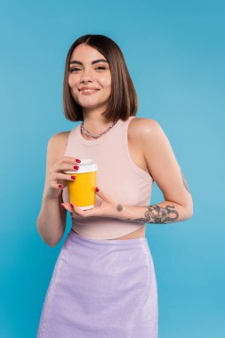 to go coffee, happy young woman with short hair, tattoos and nose piercing holding paper cup on blue background, generation z, summer trends, attractive, coffee culture, everyday style  clipart