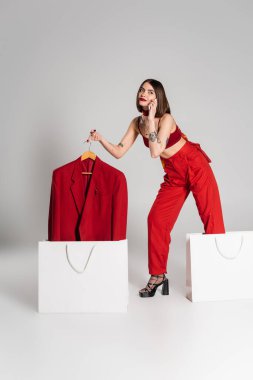 Tüketim, kısa saçlı ve burnu piercingli, spor ceketli, akıllı telefondan konuşan gri arka planda, modern moda trendi, tam boy 