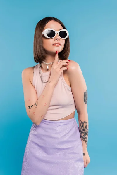 stock image fashion trend, brunette young woman with short hair in tank top, skirt and sunglasses posing on blue background, casual attire, gen z fashion, personal style, everyday makeup, casual attire 