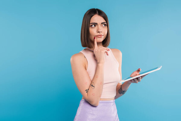 brunette young woman with short hair, tattoos and nose piercing digital tablet laptop on blue background, generation z, summer trends, attractive, social media influencers, tablet user, pensive 