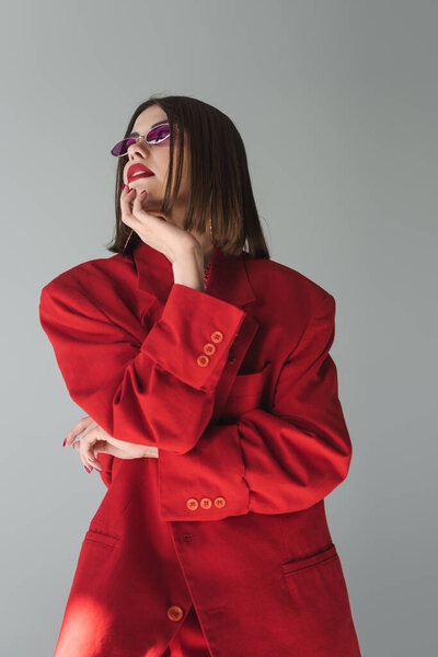 исполнительный стиль, молодая брюнетка женщина с короткими волосами позирует в розовых солнцезащитных очках и красный костюм на сером фоне, поколение z, модный наряд, модная модель, профессиональный наряд 