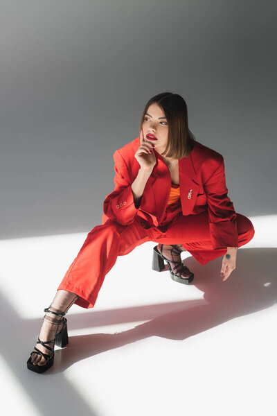 полная длина, шикарный стиль, молодая брюнетка с короткими волосами позирует в костюме на сером фоне, поколение z, модный наряд, модная модель, профессиональный наряд, исполнительный стиль, обувь на каблуках