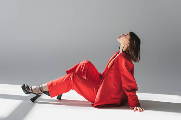 полная длина, вид сбоку, молодая брюнетка с короткими волосами позирует в костюме на сером фоне, поколение z, модный наряд, модная модель, профессиональный наряд, исполнительный стиль, туфли на каблуках