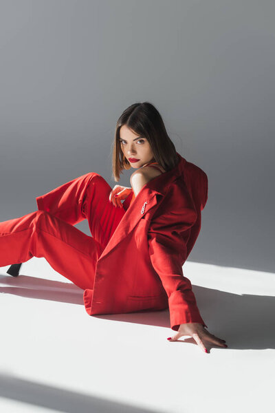 модный, молодая брюнетка женщина с короткими волосами позирует в костюме на сером фоне, поколение z, модный наряд, модная модель, профессиональный наряд, исполнительный стиль, глядя на камеру