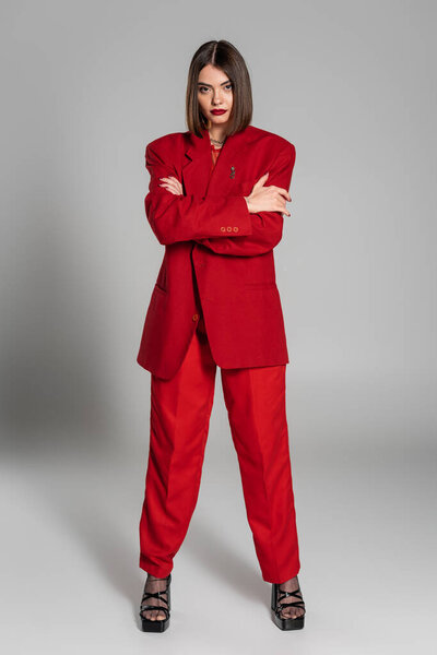 сложенные руки, молодая женщина с короткими волосами и пирсингом носа, позируя в костюме на сером фоне, поколение z, модный наряд, модная модель, профессиональный наряд, исполнительный стиль, полная длина 