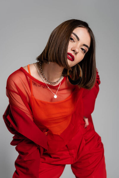 официальный наряд, молодая брюнетка женщина с короткими волосами и пирсинг носа позируя в костюме на сером фоне, поколение z, модный наряд, модная модель, профессиональный наряд, исполнительный стиль 