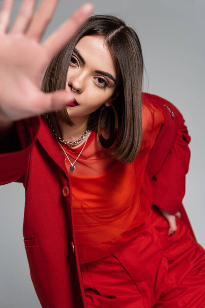 корпоративная мода, молодая брюнетка с короткими волосами позируя в костюме и протягивая руку на сером фоне, поколение z, модный наряд, модная модель, профессиональный наряд 