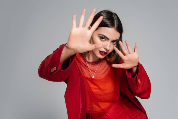 официальный наряд, молодая брюнетка женщина с короткими волосами позируя в костюме и протягивая руки на сером фоне, поколение z, модный наряд, модная модель, профессиональный наряд 