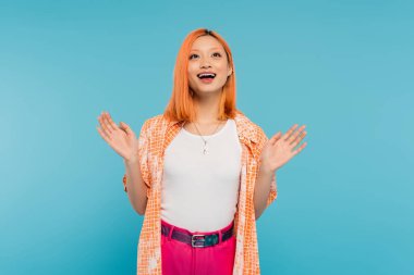 amazed asian woman, cheerful model with dyed hair smiling and gesturing with hands on vibrant blue background, opened mouth, generation z, casual attire, orange shirt, happy face, expressive  clipart