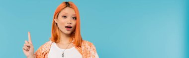 pointing with finger, amazed face, young asian woman with dyed hair showing something on camera on blue background, generation z, casual attire, young culture, expressive, website banner  clipart