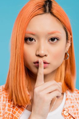 hush, young asian woman with dyed hair and eyebrows showing shh, holding finger over lips on blue background, looking at camera, secret, silence gesture, be quiet, generation z, portrait  clipart