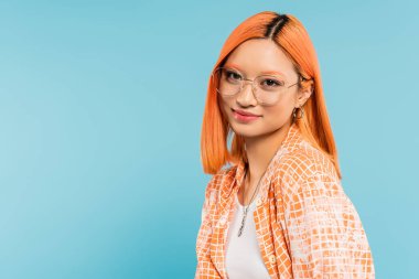 youthfulness and happiness, pretty asian woman with colored red hair, in fashionable eyeglasses and orange shirt smiling at camera on blue background, generation z, summer vibes clipart