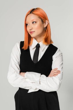 Beyaz gömlekli, siyah kravatlı ve yelekli genç ve çekici Asyalı manken çapraz kollu ve gri arka planda duruyor, modern iş modası, Z jenerasyonu.