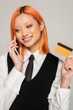Mutlu duygular, renkli kızıl saçlı neşeli Asyalı kadın ve ışıl ışıl gülümseyen akıllı telefondan online sipariş veren gri arka plan, iş modası, siyah beyaz elbiseler
