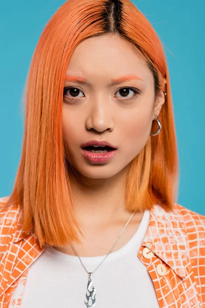 shocked face, young asian woman with red hair looking at camera and standing with open mouth on blue background, casual wear, generation z, emotional, wow, surprised, astonished