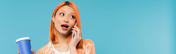 phone call, open mouth, asian and young woman with red hair holding takeaway drink and talking on smartphone on blue background, casual attire, generation z, coffee culture, amazed, banner