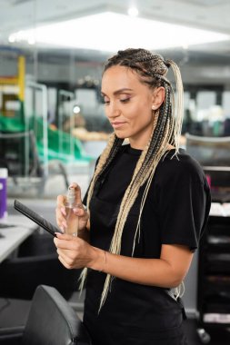 Kuaför saç tarağı dezenfekte ediyor, sprey tutuyor, saç örüyor, kuaförde çalışıyor, temizlik malzemeleri, hijyen, berber dükkanı, güzellik, temizlik, küçük işletmeler. 