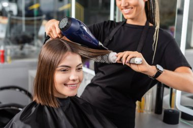 Pozitiflik, kuaför, saç fırçası ve saç kurutma makinesi olan profesyonel kuaför bayan müşterinin saçı, kısa saçlı mutlu esmer kadın, güzellik salonu, saç kesimi, fön. 