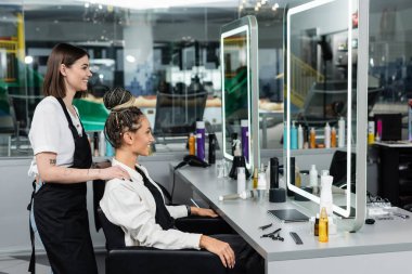 Müşteri memnuniyeti, kuaför deneyimi, mutlu saç stilisti ve aynaya bakan kadın müşterisi, neşeli kadınlar, saç çöreği, kuaför salonu müşterisi, güzellik servisi, dövme, yan görüş 